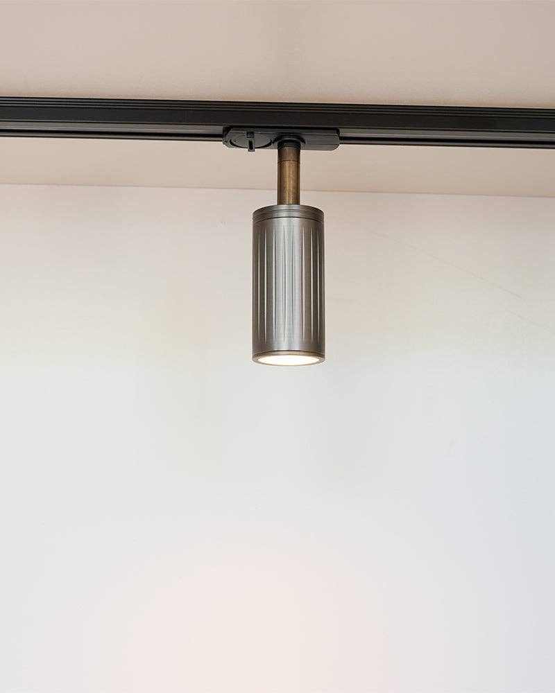 Luminar browned brass ribbed spotlight hanging from a black track, lit