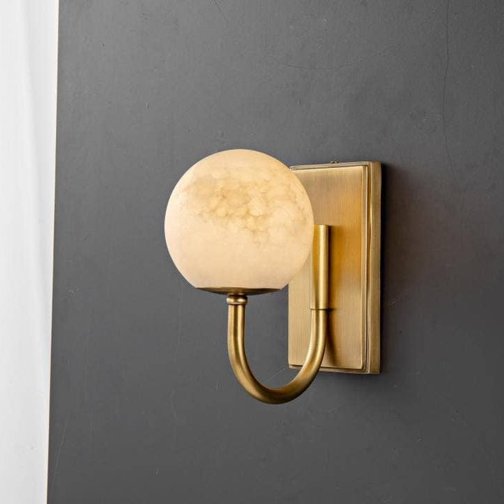 Alabaster globe wall light in satin brass lit against a charcoal panel