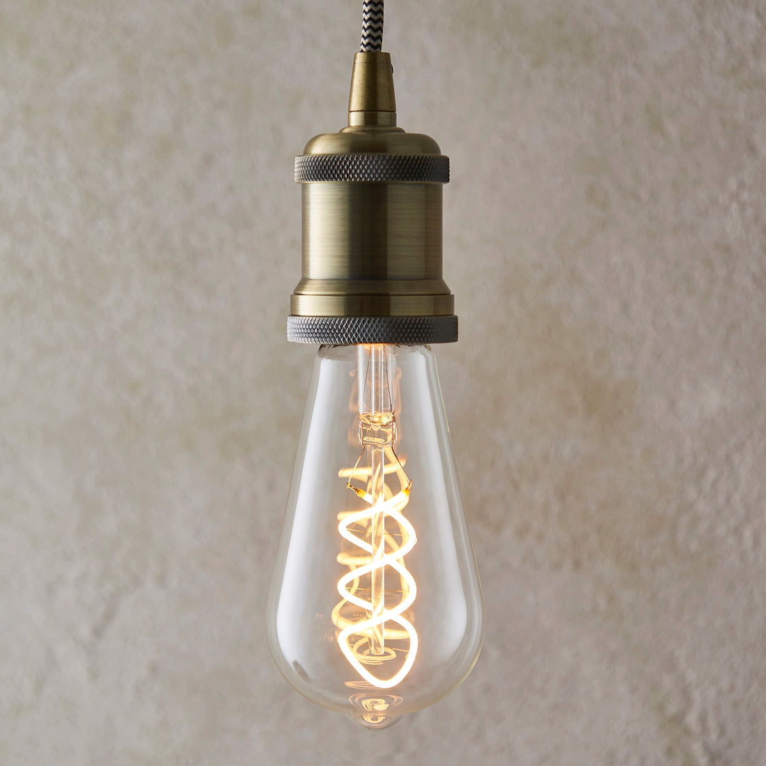 Helios spiral filament bulb lit in an industrial bronze pendant against plaster