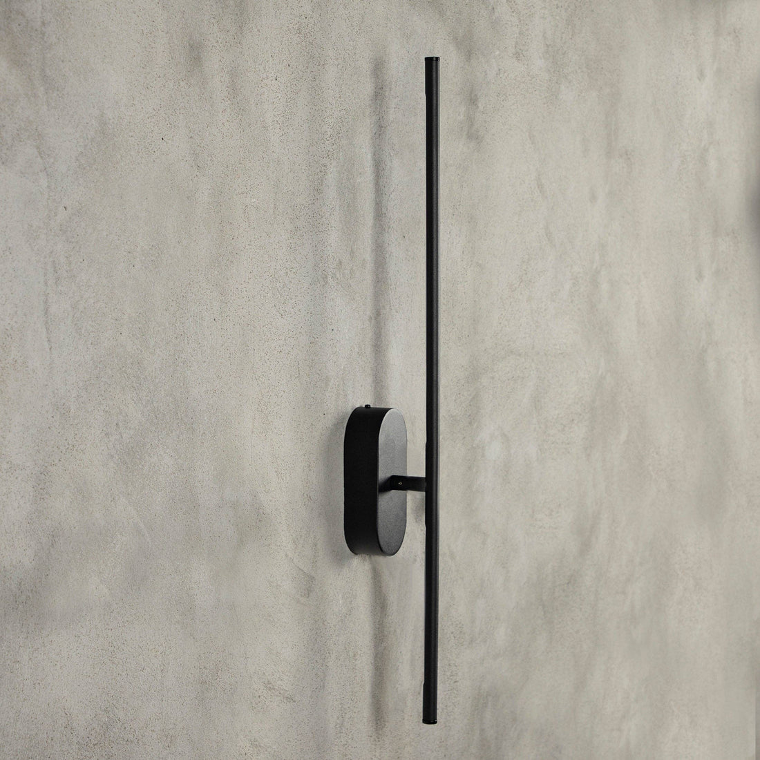 Assos 70cm matt black bar light mounted vertically on raw plaster, unlit