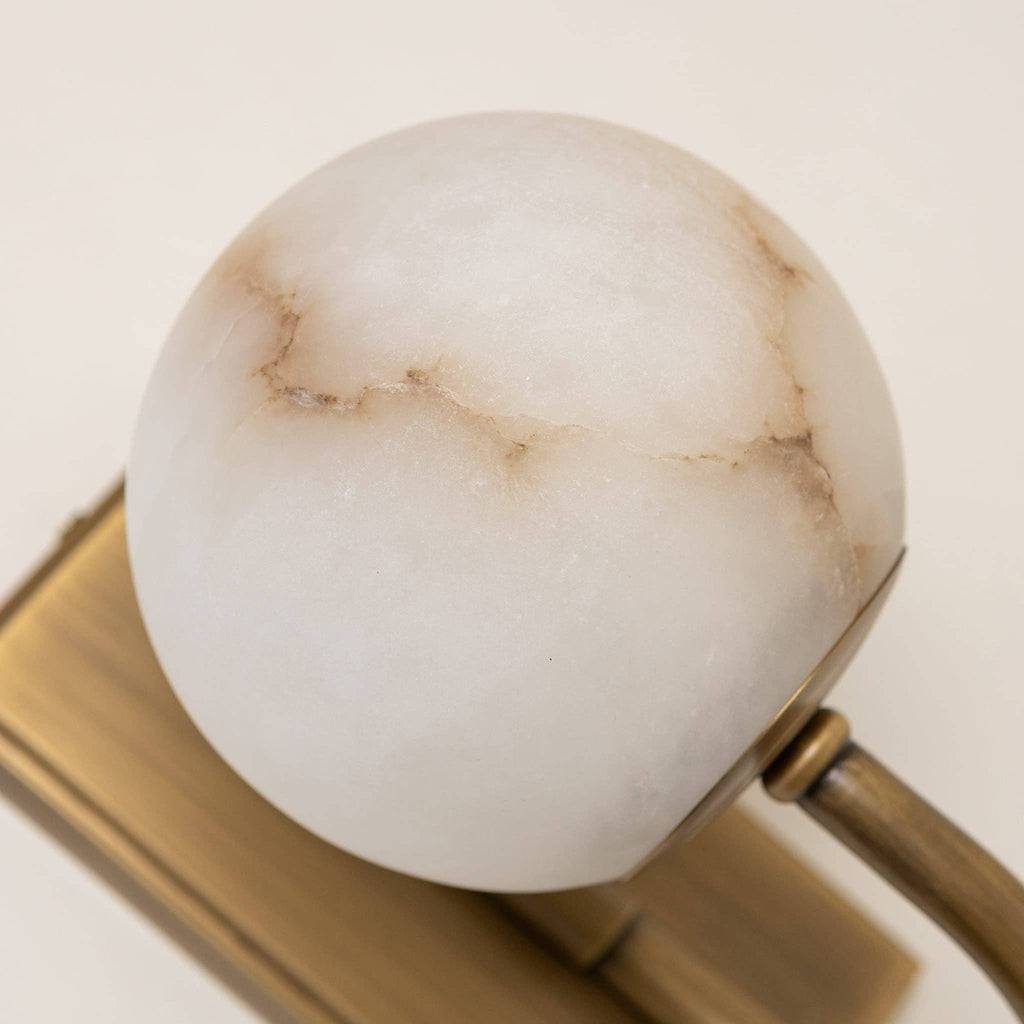Antique brass and alabaster wall light illuminated in interior setting