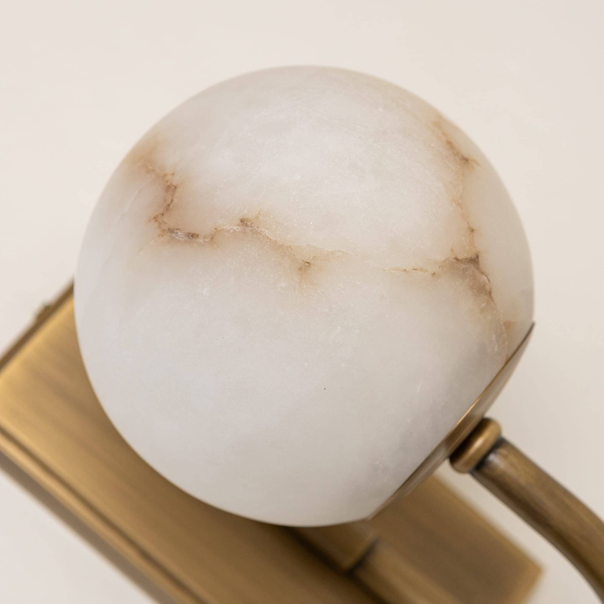 Antique brass and alabaster wall light illuminated in interior setting