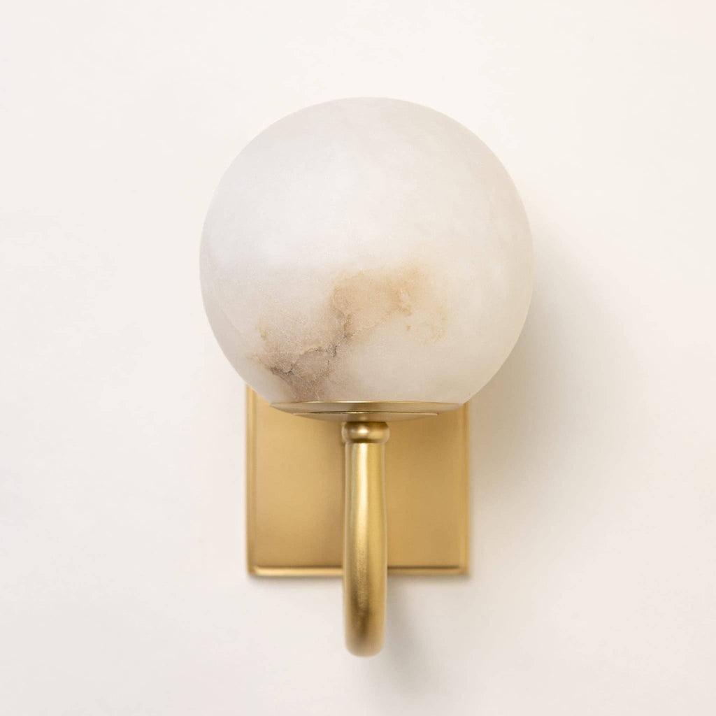 Satin brass alabaster wall light illuminated showing warm ambient glow