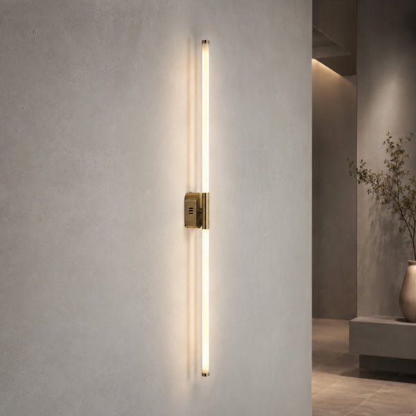 Akra 100cm vertical LED tube wall light in antiqued metal lit in a plaster hallway