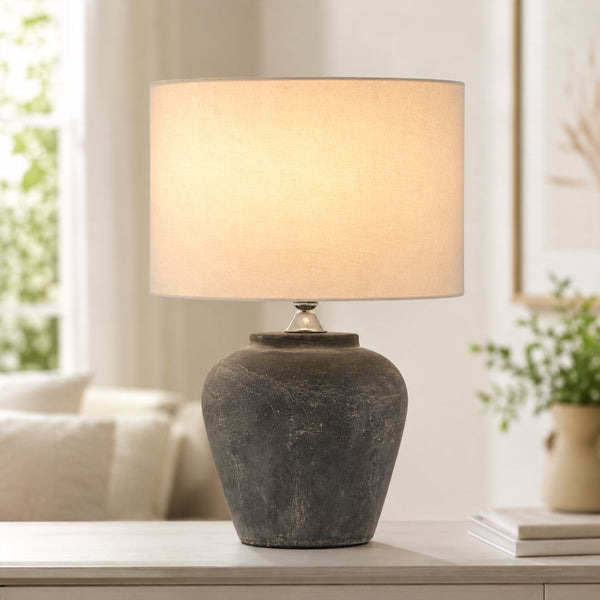 Amalfi grey stone-effect urn table lamp with linen shade lit on a side table