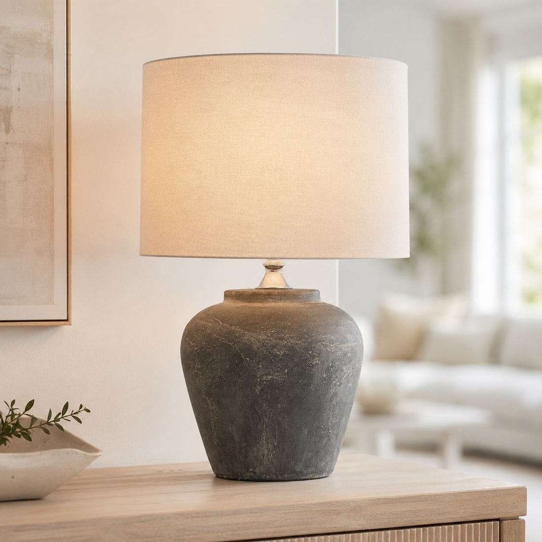Amalfi grey stone-effect table lamp lit on a side table by a window