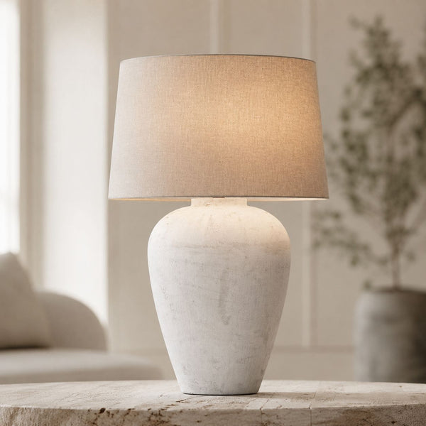Athena tall aged stone table lamp with linen shade on a side table with greenery