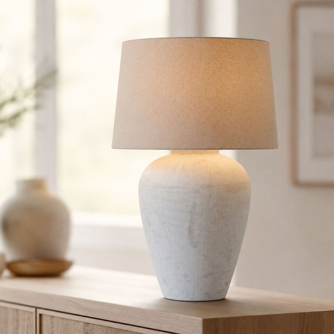 Athena aged stone table lamp lit on a side table by a window