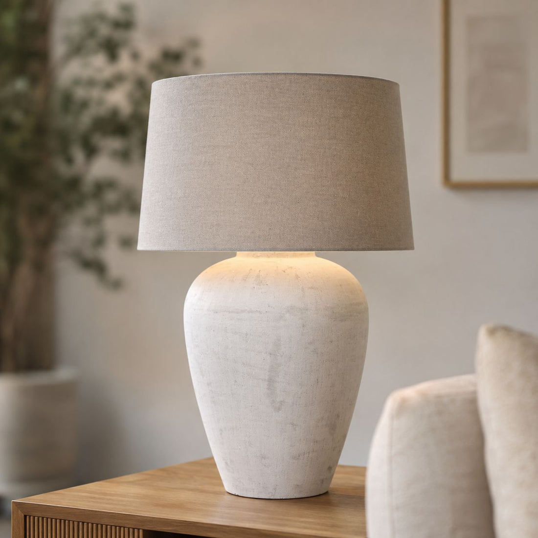 Athena tall aged stone table lamp with linen shade on a console with an armchair
