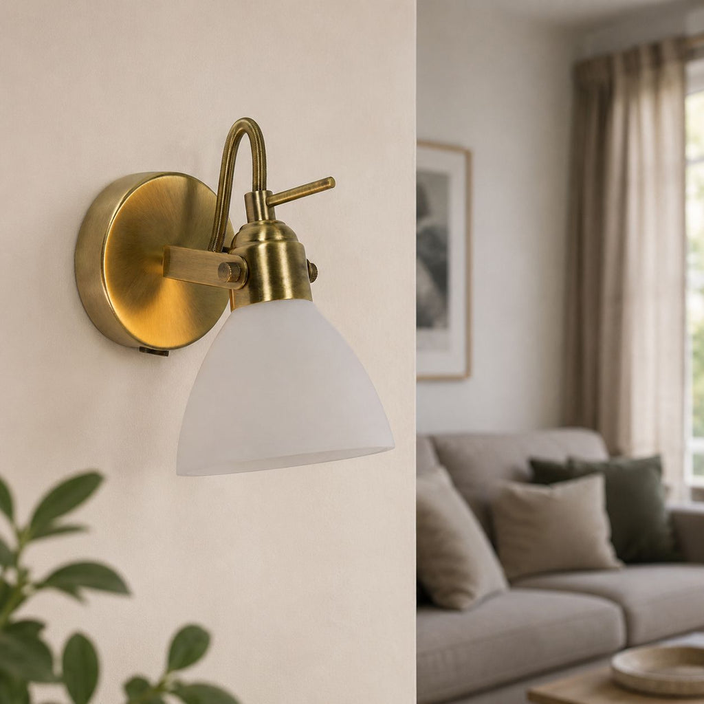 Callas antique brass wall spot light with opal glass shade lit in a living room