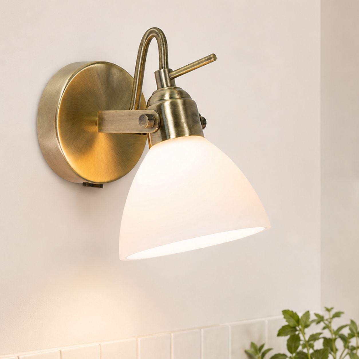 Callas antique brass wall spot light with opal glass shade, lit on a white wall