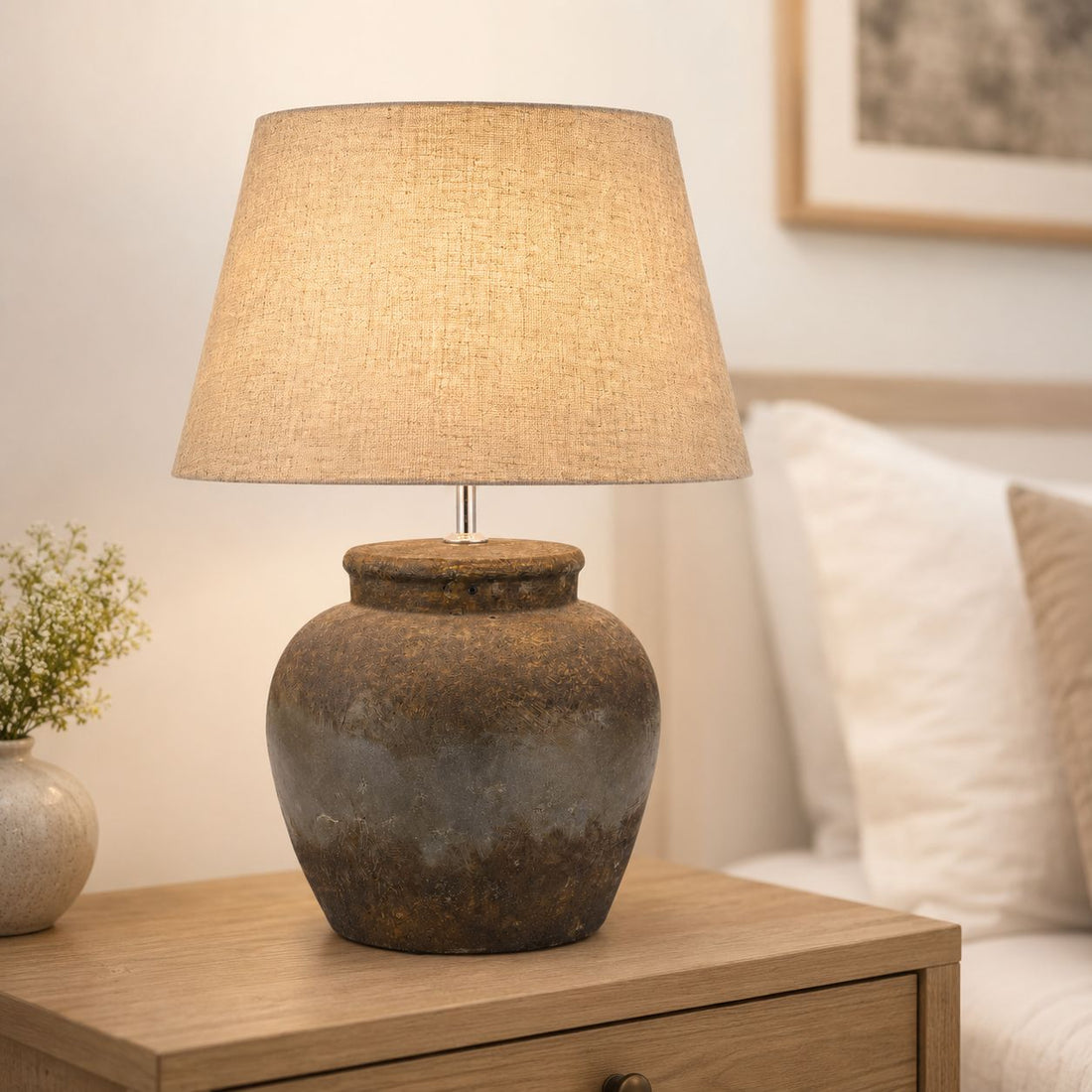 Castello aged stone table lamp lit on a sideboard with a cream sofa behind