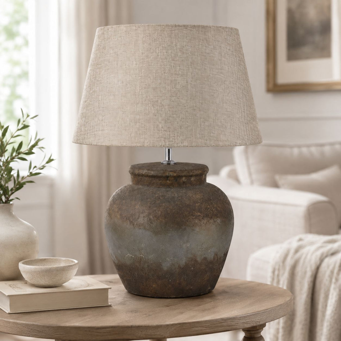 Castello aged stone table lamp on a console table beside a sofa in a neutral living room