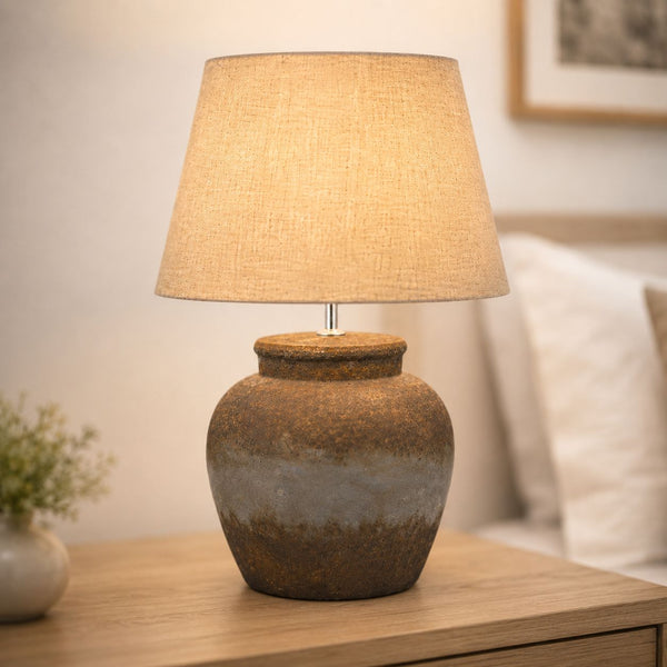 Castello aged stone urn table lamp with linen shade lit on a wooden side table