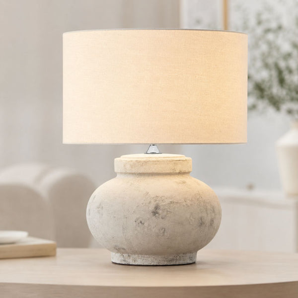 Darcy squat antique white stone-effect table lamp with linen drum shade on a side table