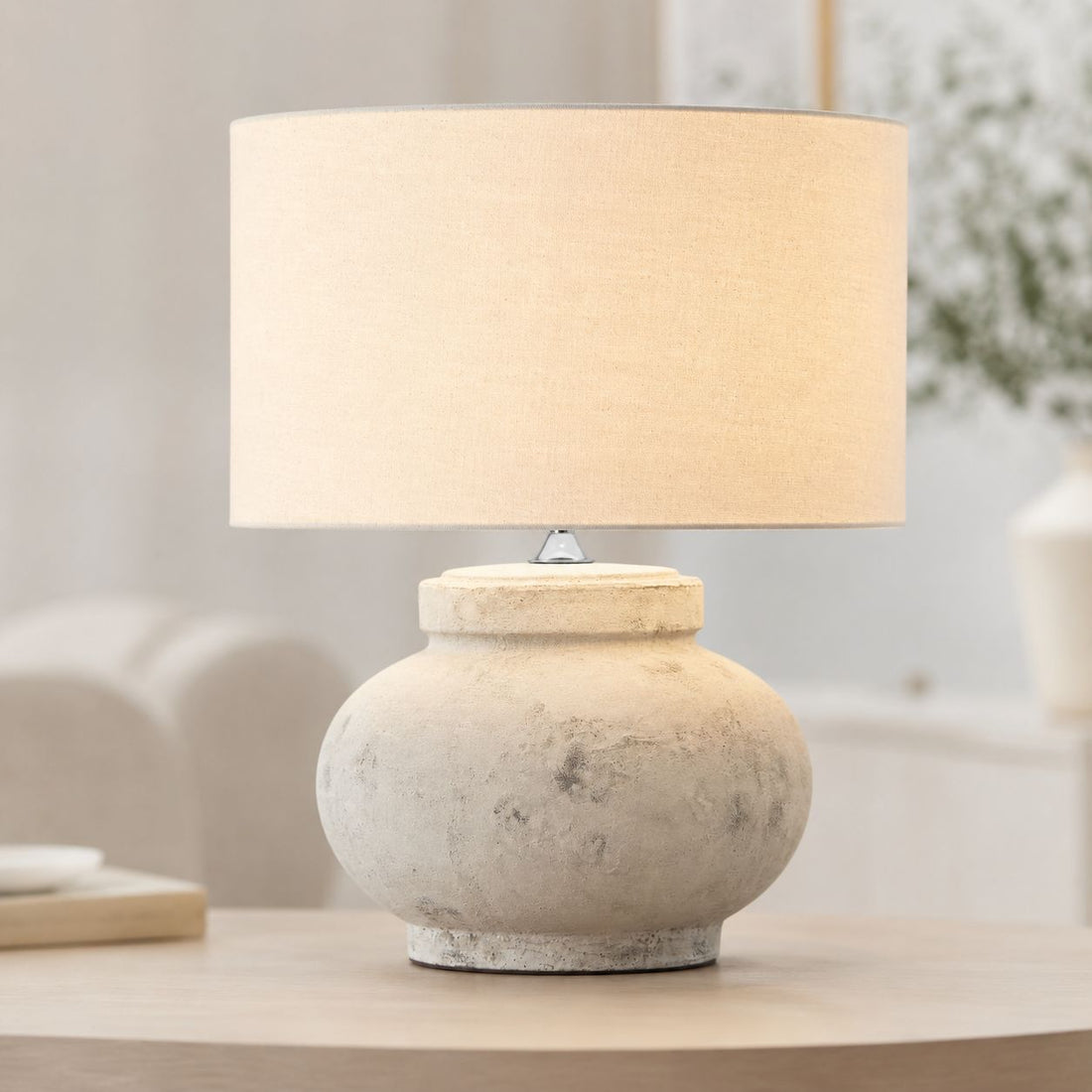 Darcy squat antique white stone-effect table lamp with linen drum shade on a side table