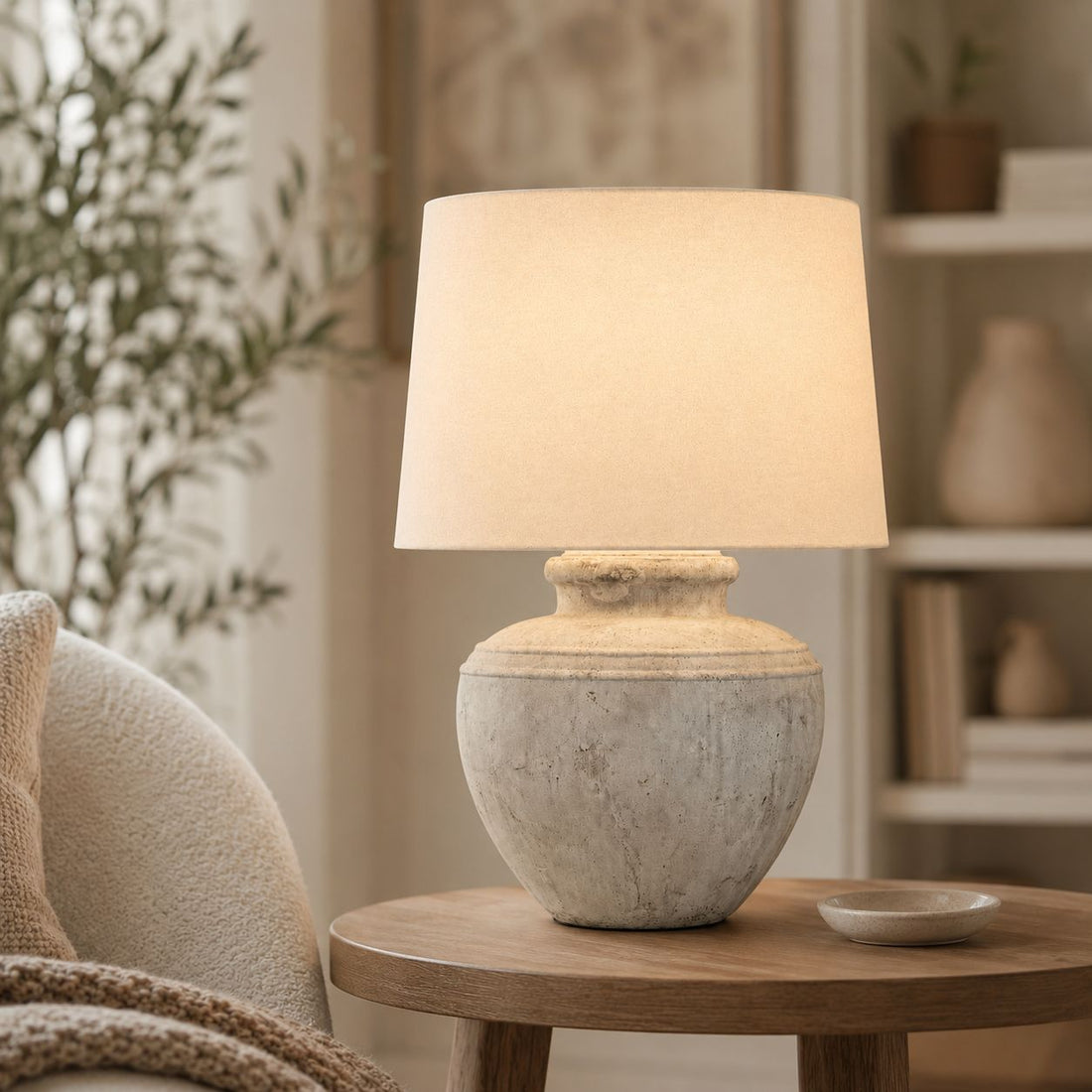 Darcy Chorus antique white stone lamp lit on a side table beside a sofa