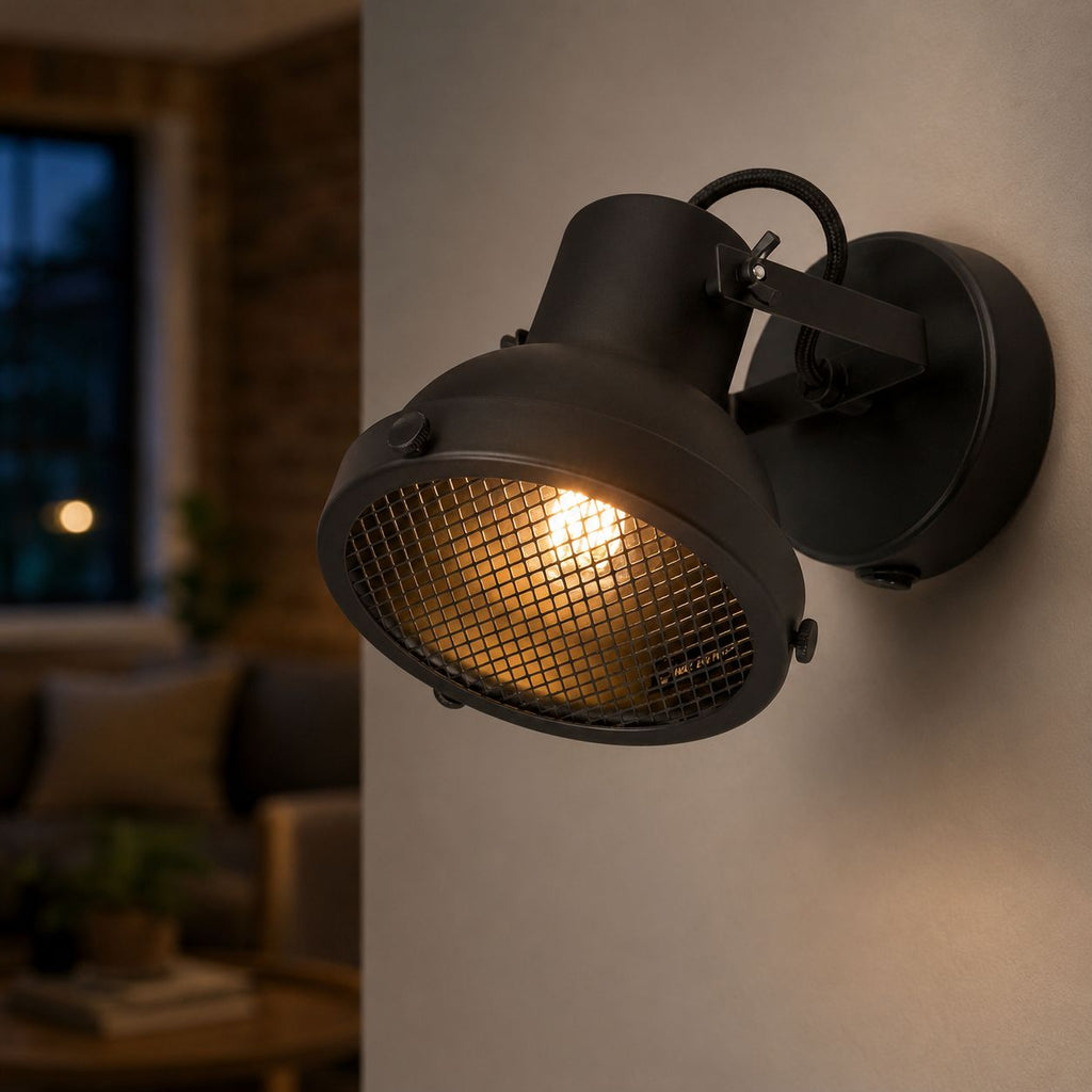 Forge black caged wall spotlight lit on a wall at night