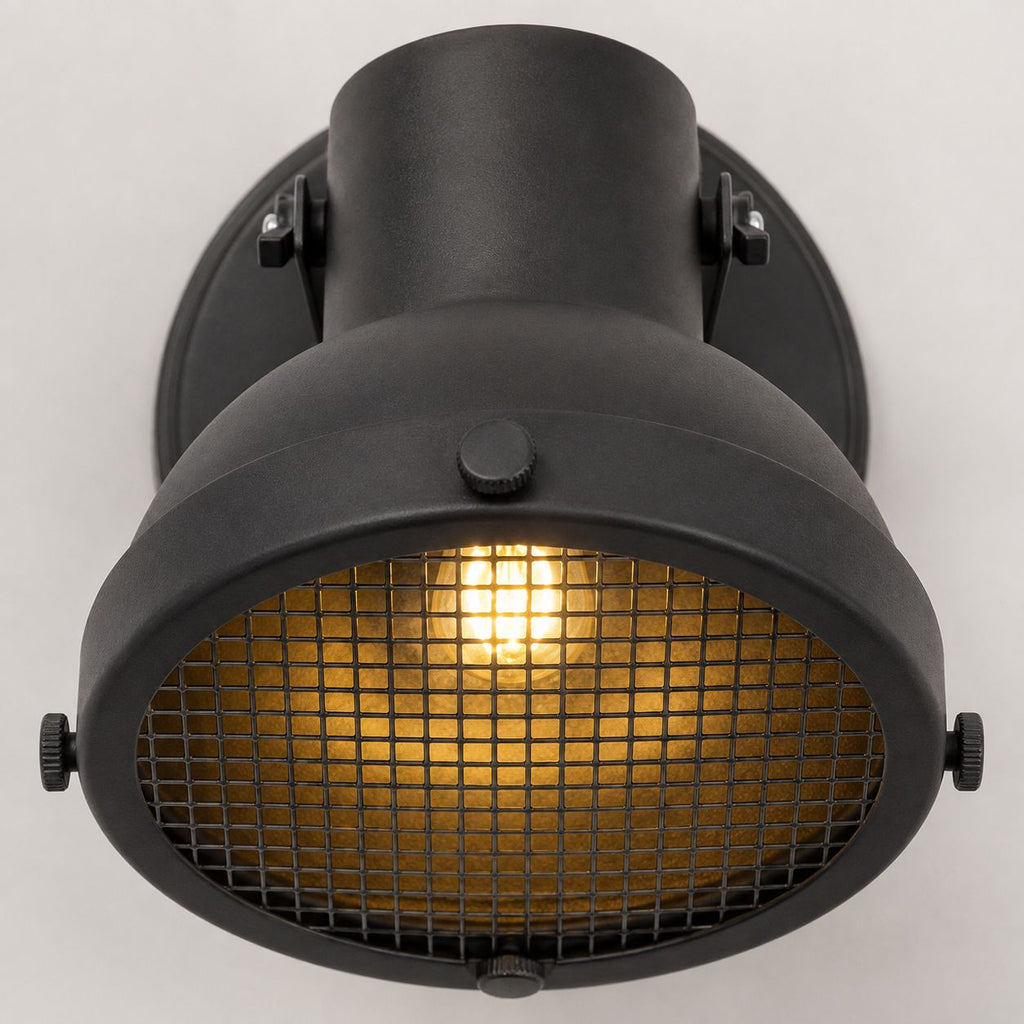 Forge caged wall spot light, close-up of the black mesh grille and lit bulb