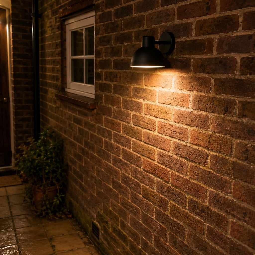 Hadsten black down light lit against a brick wall beside a window