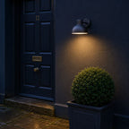 Hadsten matt black outdoor wall light lit beside a navy front door at night