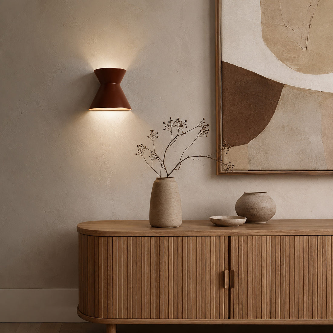 Small Kiro cocoa sconce lit beside earthy abstract art over a sideboard