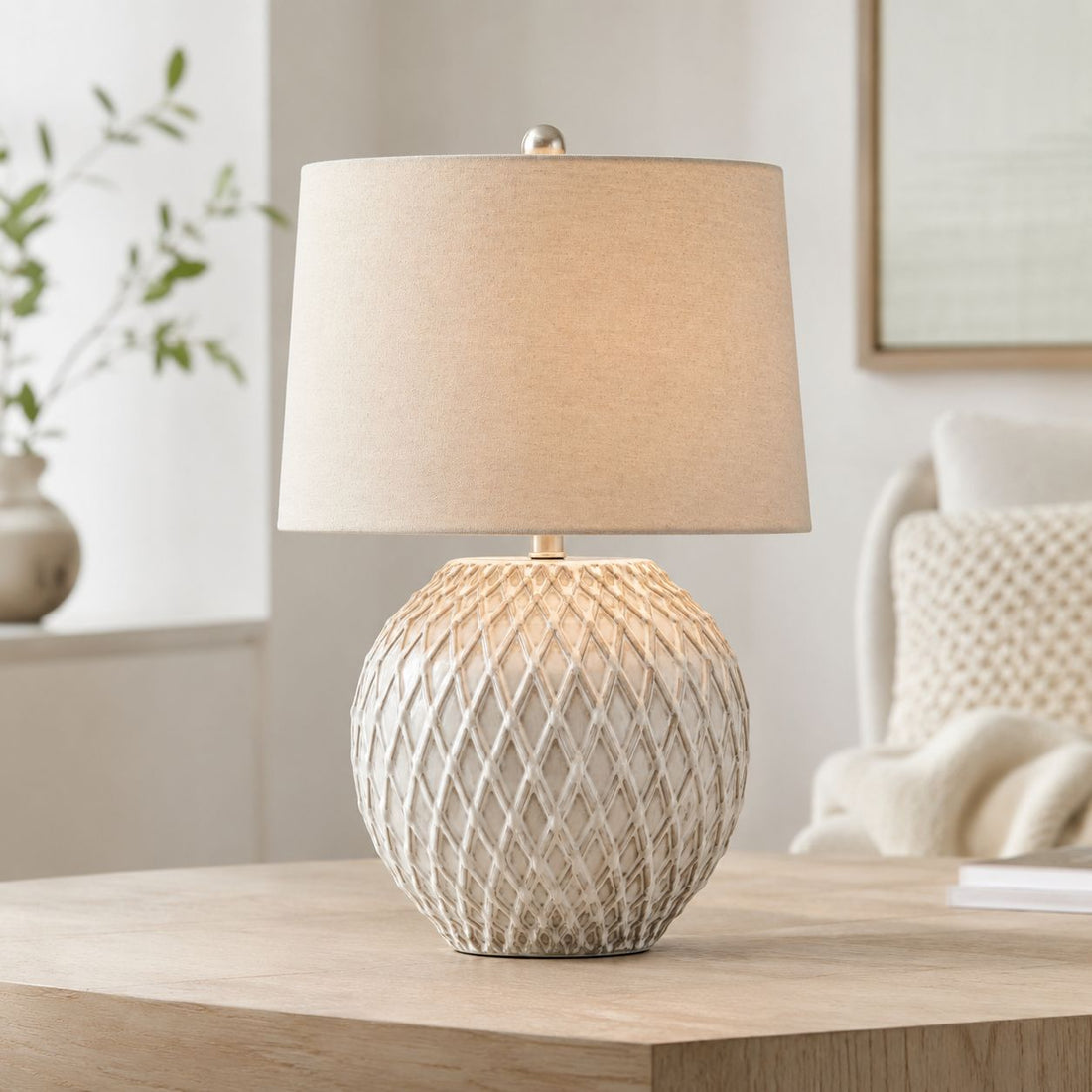 Lattice ceramic table lamp with cream linen shade on a bedside table with plants