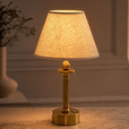 Lira brass cordless table lamp with oatmeal shade lit on a table by a window