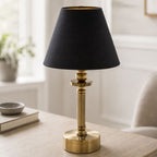 Lira cordless brass table lamp with black shade on a coffee table in a living room