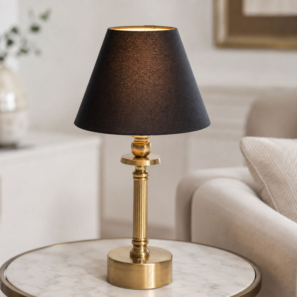 Lira brass rechargeable table lamp with black shade on a side table beside a sofa