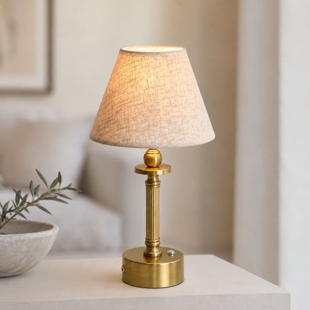 Lira brass cordless lamp with oatmeal shade on a white side table with olive branch