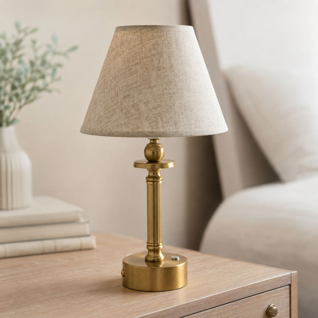 Lira brass rechargeable table lamp with oatmeal shade on a wooden bedside table