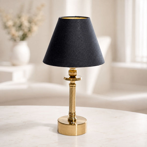 Lira rechargeable brass table lamp with black tapered shade on a white side table