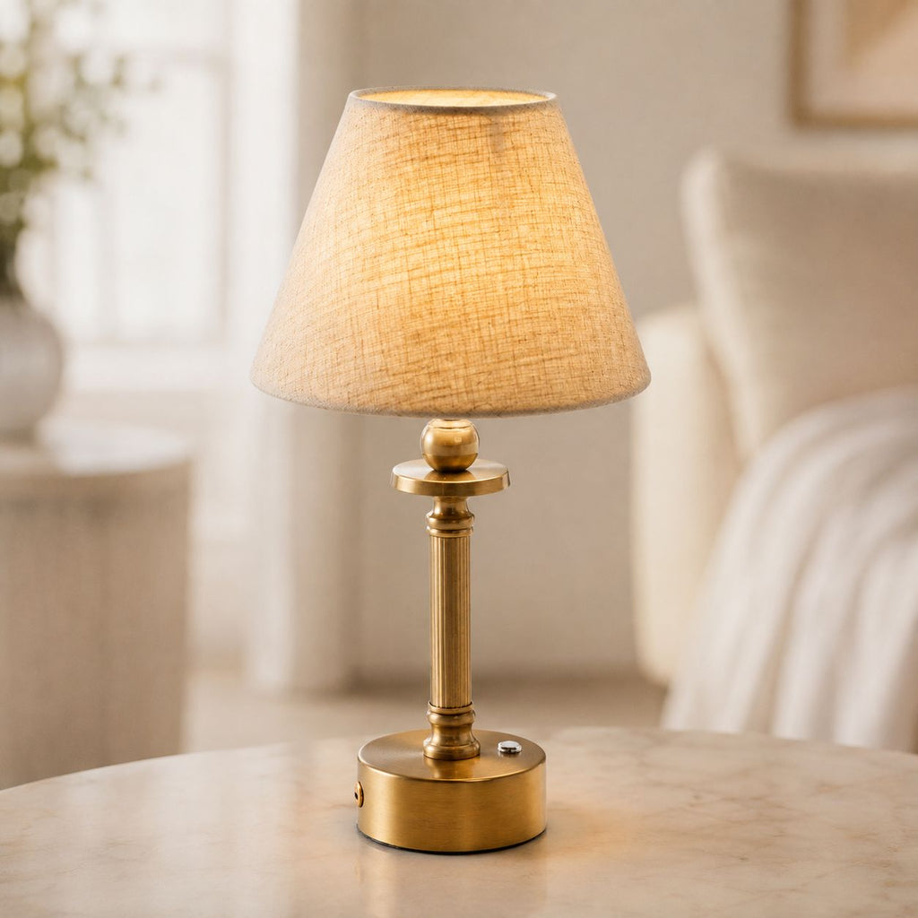 Lira brass cordless table lamp with oatmeal linen shade lit on a side table