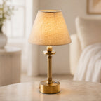 Lira brass cordless table lamp with oatmeal linen shade lit on a side table