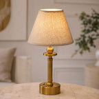 Lira brass rechargeable lamp with oatmeal shade on a side table beside an armchair