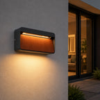 Loren wood and anthracite LED wall light lit on an exterior wall beside glazed doors at dusk
