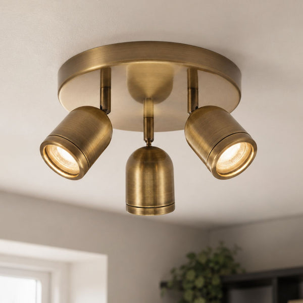 Lucca antique brass triple spot bathroom ceiling light lit on a white ceiling