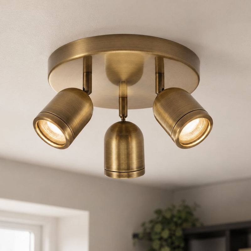 Lucca antique brass triple spot bathroom ceiling light lit on a white ceiling