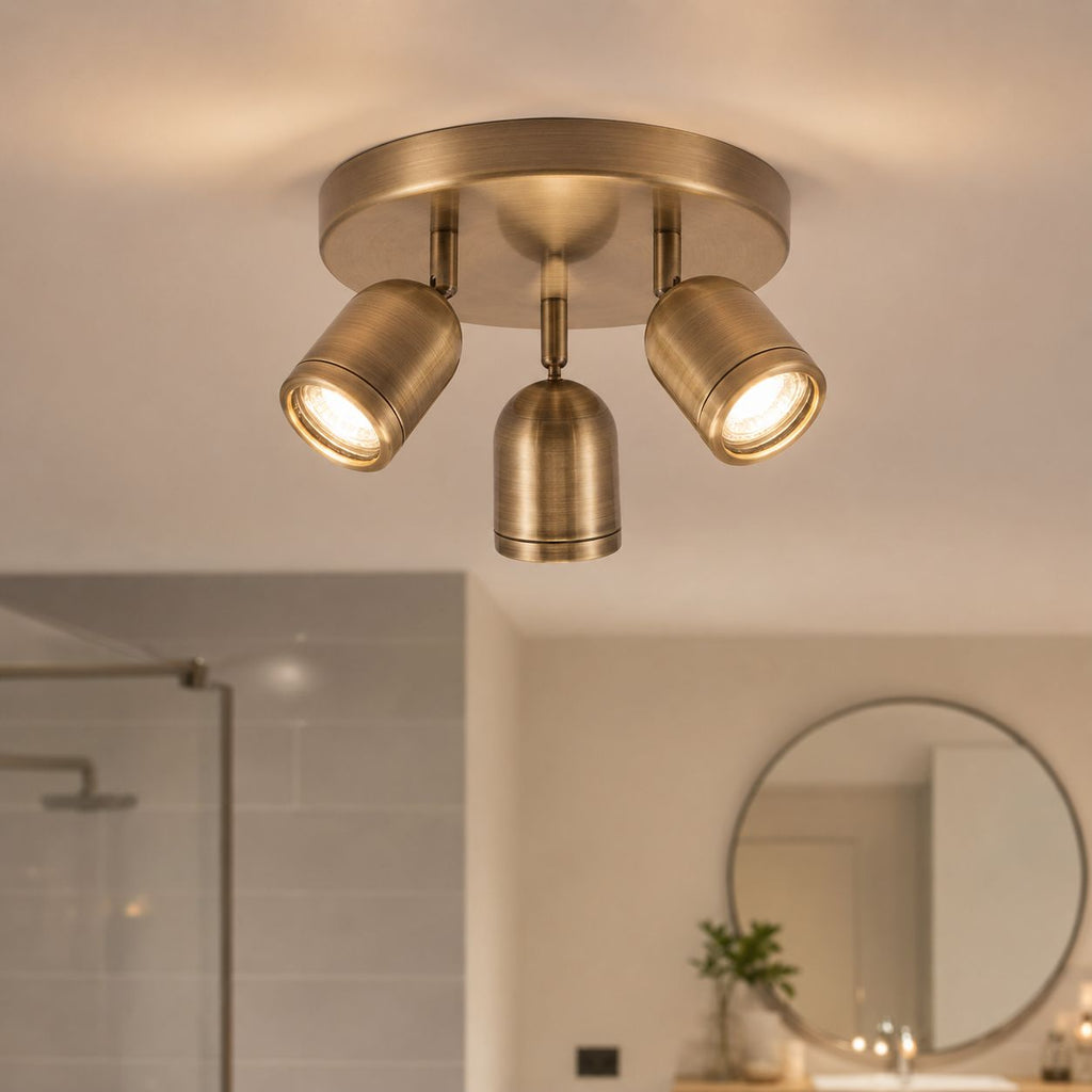 Lucca antique brass three-spot ceiling light in a bathroom with round mirror