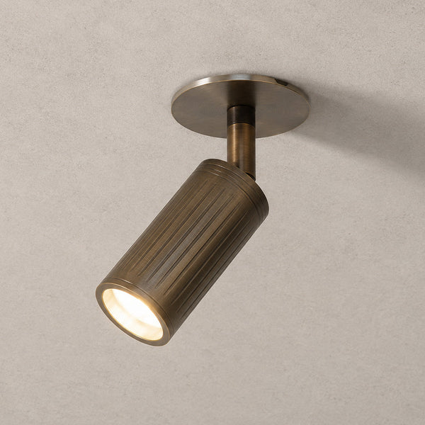 Luminar browned brass ceiling spotlight tilted, lit with warm beam