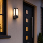 Lyon black sensor wall light lit on a house wall beside a dark front door at night
