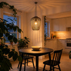 Riva light grey cage pendant lit over a round dining table by a window at dusk