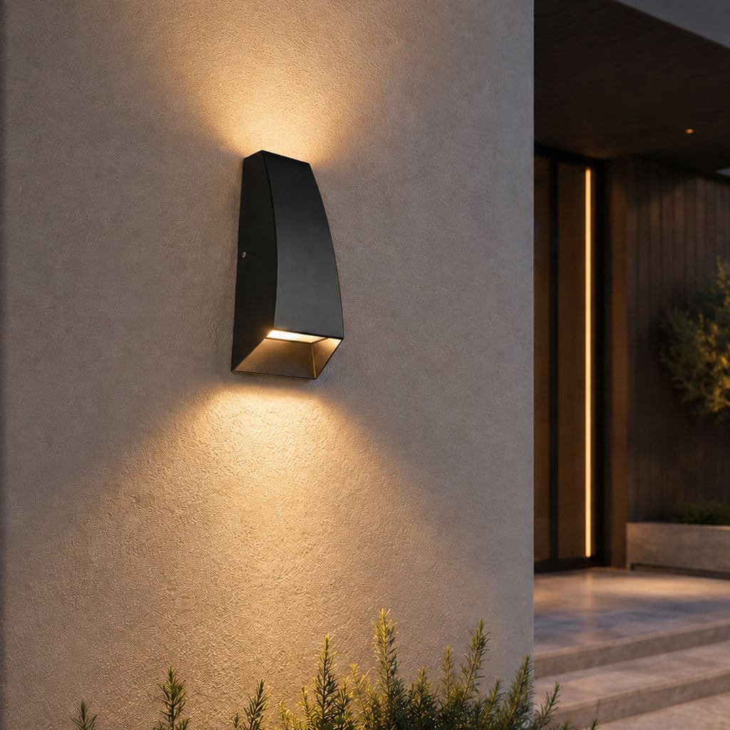 Silas black wedge outdoor wall light casting a downward glow on a rendered wall at dusk