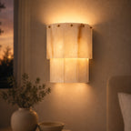 Valora tiered alabaster wall sconce with brass studs glowing at dusk