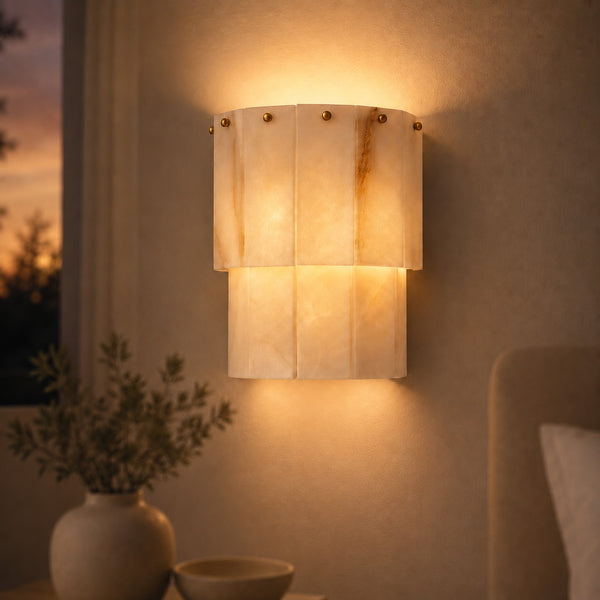 Valora tiered alabaster wall sconce with brass studs glowing at dusk