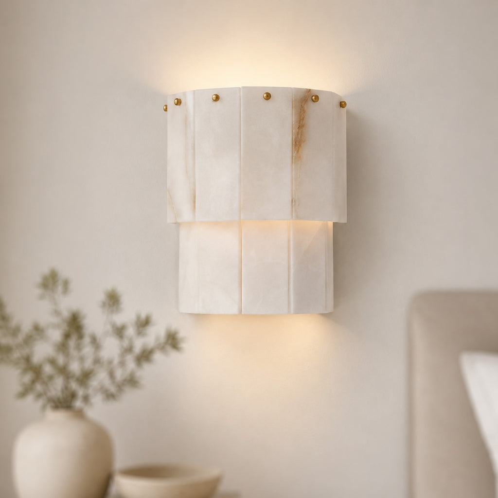 Valora tiered alabaster wall light glowing beside a cream headboard