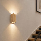 Talia wood-effect up down wall light lit on a white hallway wall by a staircase