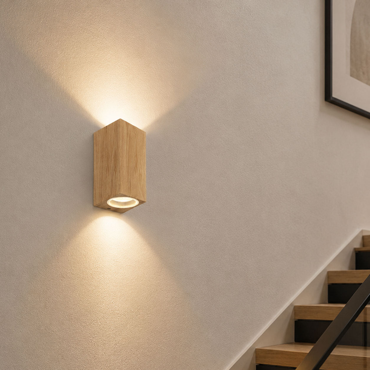 Talia wood-effect up down wall light lit on a white hallway wall by a staircase