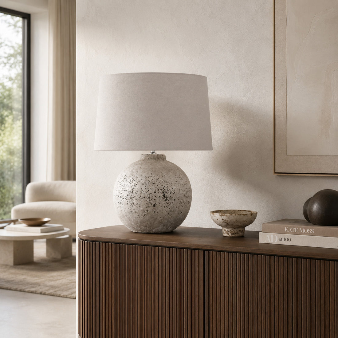 Tiber round stone table lamp on a dark ribbed cabinet in a cream lounge